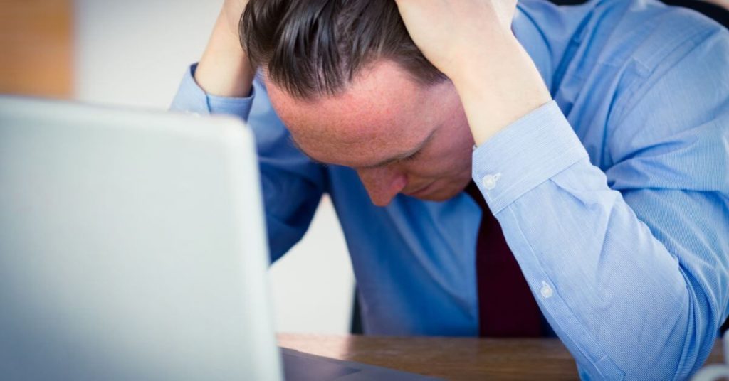 A business man is stressed in front of his laptop while looking over insurance claims