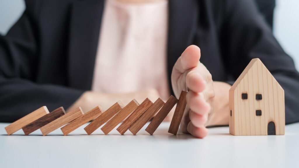 falling blocks on house with hand stopping symbolizing risk reduction for home disasters