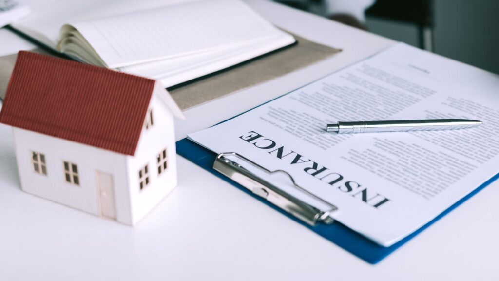 A home insurance claim form on a desk with a small home replica
