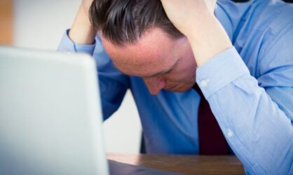 A business man is stressed in front of his laptop while looking over insurance claims